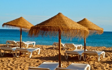 Fototapeta na wymiar Straw umbrellas with sunbeds at the beach and sea