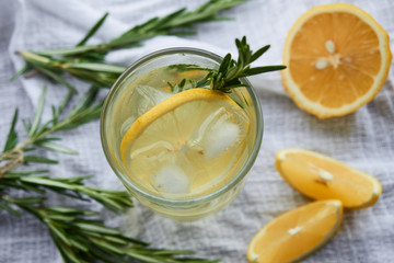 a glass of lemonade with a slice of lemon and rosemary on a white napkin top view