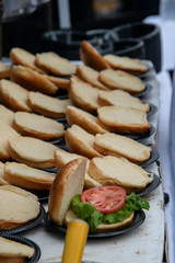 Rows of opened hamburger buns on a table. Only one had lettuce and a slice of tomato on it