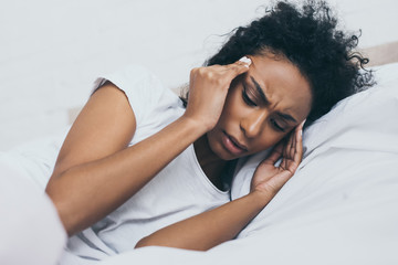 pretty african american woman suffering from headache while lying in bed