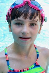 Portrait of a wet girl in a pool with goggles on her forehead