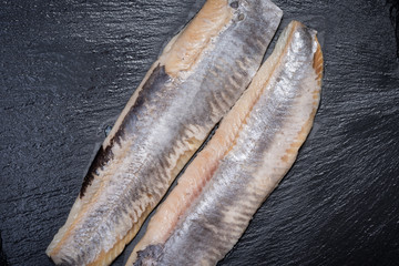 Salted boneless fillets of wild-caught Atlantic Herring arranged on natural black stone background. Clupea harengus.
