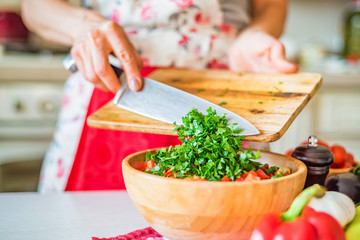 Female hand put chopped parsley in wooden bowl with salad in kitchen. Cooking vegetables
