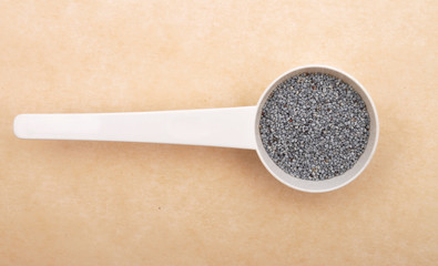 Mohn in Dosierlöffel auf braunem Hintergrund