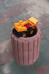 Broken toy yellow car thrown into the garbage can in the yard on a summer day