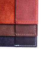 Three handmade leather passport covers stack isolated on white background. Closeup view. Covers are dark blue, red, brown and opened.
