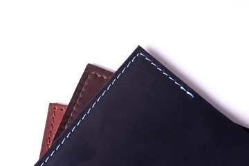 A parts of three handmade leather passport covers isolated on white background. Closeup view. Covers are dark blue, red and brown.