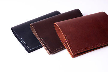 Three handmade leather passport covers isolated on white background. Covers are closed. Closeup view. Covers are dark blue, red and brown.