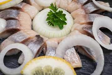 Hollandse Nieuwe- Traditional Dutch Food. Soused raw Herring soaked in mild marinade. Garnished with Lemon, Onion and Parsley on black natural stone.