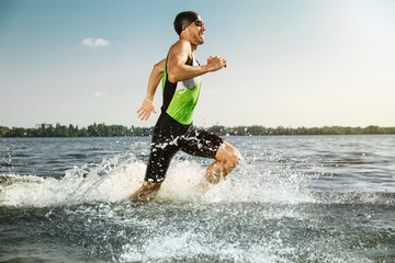 Professional triathlete swimming in river's open water. Man wearing swim equipment practicing triathlon on the beach in summer's day. Concept of healthy lifestyle, sport, action, motion and movement. - obrazy, fototapety, plakaty