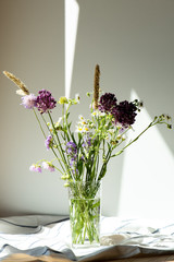Bouquet of meadow flowers in a glass vase on the table, light background.
