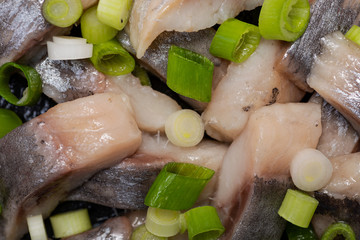 Slices of Salted Boneless wild-caught Atlantic Herring garnished with Chopped Green Onion Scallions. Black natural stone background. Clupea harengus. 