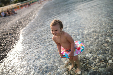 child bathes in the sea, pebble beach, cloudy