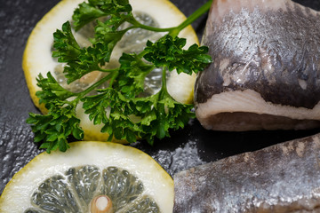 Salted Deboned Herring Fillets garnished with Yellow Onion, Lemon and Fresh Parsley. Natural black stone background. Clupea harengus.