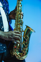 Young african-american jazz musician playing the saxophone on blue studio background in trendy neon...