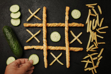 Game of tic tac toe of french fries and cucumber. Choosing healthy vs unhealthy foods. Fit or fat concept.