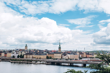 Scenic summer panorama of the Old Town (Gamla Stan) architecture in Stockholm, Sweden. view from Monteliusvagen hill on island Riddarholm and tower of church. Lake Malaren with blue sky, white clouds.