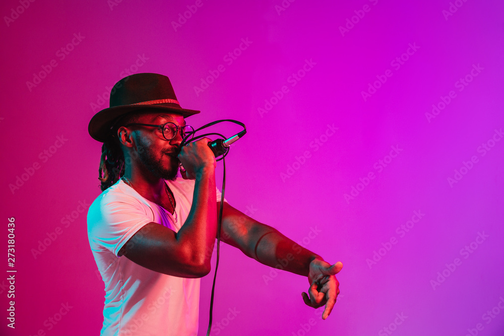 Wall mural young african-american jazz musician with microphone singing a song on purple studio background in t