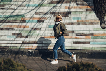 Beautiful Blonde Girl in Green Jacket Listening Music in Headphones