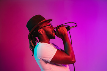 Young african-american jazz musician with microphone singing a song on purple studio background in...