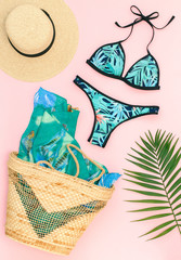 Bikini swimsuit with tropical print, straw hat, wicker beach bag, sarong and tropical date palm...