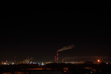 Night shot of the oil refinery on the city skyline. Lots of lights. Industrial and residential areal. Air Pollution and Climate Change.Smoke from the pipes of the factory