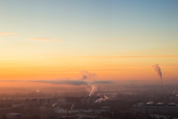 Sunrise over factory at the industrial area. Orange light rays comes through morning fog and smoke from pipes. Power plant
