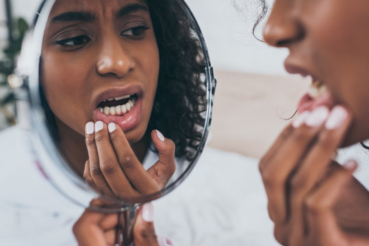 young african american woman looking at mirror while suffering from tooth pain