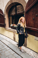 The girl walks with a camera in Prague. A young blonde woman walks along a narrow cobbled street in Prague, Czech Republic. Stylish blonde girl in a leather jacket.