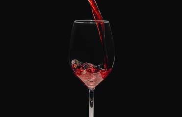 Pouring wine into a glass against a dark background. Red wine is poured into the glass, isolated on a black background. The concept of alcohol consumption, food, restaurants.
