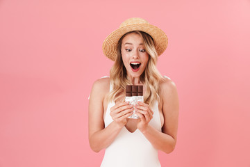 Happy excited young woman posing isolated over pink wall background dressed in swimwear beach concept holding chocolate.