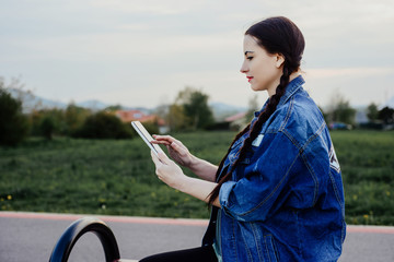 Writing and using a tablet by a woman. A woman sitting outside on a bench and browses the...