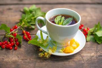 white cup with tea on a wooden table, around a berry, strawberry, mint