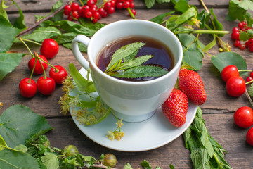 white cup with tea on a wooden table, around a berry, strawberry, mint