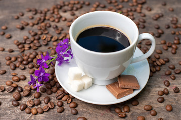 white cup of coffee on a wooden table, chocolate, sugar and coffee beans,