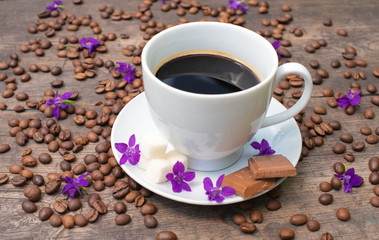white cup of coffee on a wooden table, chocolate, sugar and coffee beans,
