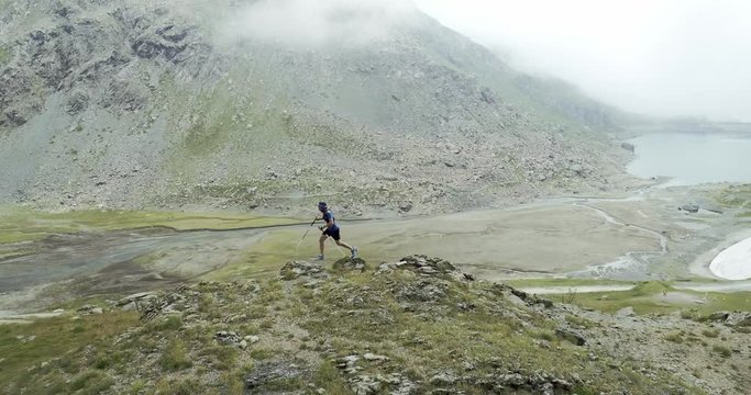 Aerial of man running on mountain rise.Trail runner running to top peak training on rocky climbing.Wild green nature outdoors in cloudy foggy bad weather. Activity,sport,effort,challenge,willpower.