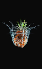 Fresh and delicious pineapple isolated against dark, black background. Pineapple dropping in water and creating a splash. The concept of healthy eating, consuming fruit.