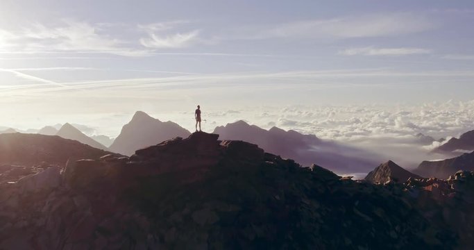 Aerial trail runner man standing on mountain top peak goal looking horizon view.drone shot.Wild nature outdoors at sunrise or sunset backlit.Training activity,sport,effort,challenge,willpower concepts