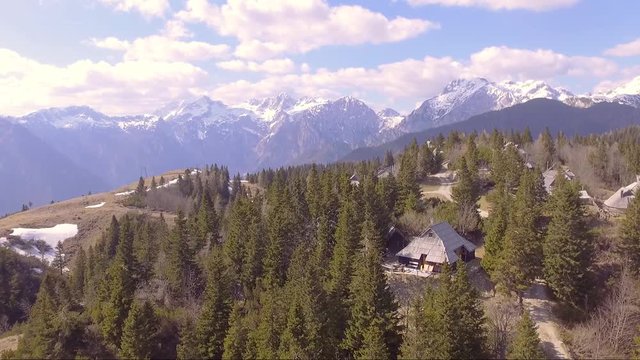 Fast flying over the beautiful Velika planina full of spruce, little houses and mountains in the back. Aerial camera shot. Landscape panorama sunny day. Slovenia