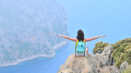 Happy girl with backpack takes hands up like a plane and enjoys beautiful sea and mountain view