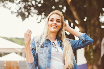 Portrait of a beautiful young woman. She is outdoors stirring her blond hair. Woman with smile on...