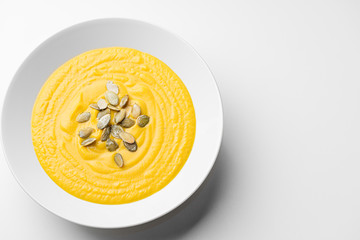 Pumpkin soup with seeds. White plate on white background. Food photography	