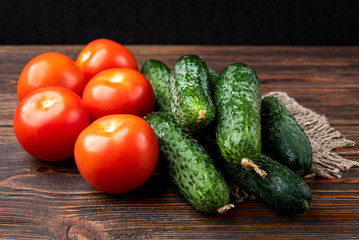 Fresh cucumbers and tomatoes on dark wooden background.