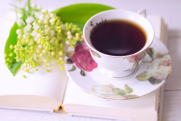 bouquet of lilies of the valley, a Cup of hot coffee and a book to relax at home. background with a book and a cup of coffee on the table close-up.
