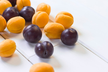 ripe plums and apricots on a white wooden background