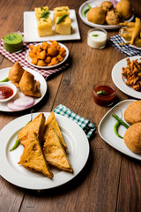 Indian Tea time snacks  in group includes Veg Samosa, Kachori/kachaudi, aloo bonda, khaman dhokla, bread, onion,chilli and moong pakora/pakoda/bhaji/bhajji/Bhajiya/bajji with sauces, selective focus