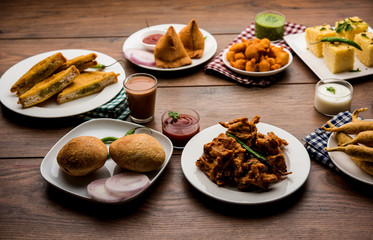 Indian Tea time snacks  in group includes Veg Samosa, Kachori/kachaudi, aloo bonda, khaman dhokla, bread, onion,chilli and moong pakora/pakoda/bhaji/bhajji/Bhajiya/bajji with sauces, selective focus