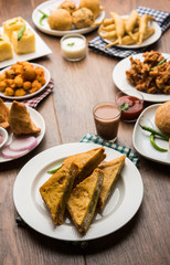 Indian Tea time snacks  in group includes Veg Samosa, Kachori/kachaudi, aloo bonda, khaman dhokla, bread, onion,chilli and moong pakora/pakoda/bhaji/bhajji/Bhajiya/bajji with sauces, selective focus