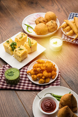 Indian Tea time snacks  in group includes Veg Samosa, Kachori/kachaudi, aloo bonda, khaman dhokla, bread, onion,chilli and moong pakora/pakoda/bhaji/bhajji/Bhajiya/bajji with sauces, selective focus